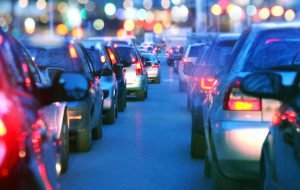 Driving a car in a city with a traffic jam at night, proceeding slow in a line of cars with red tail lights during the rush hour. view from inside the car. Blurred streets lights on the background.